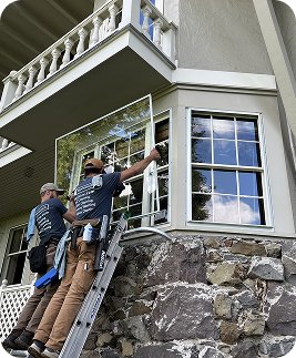 Two men providing window cleaning service on large house window